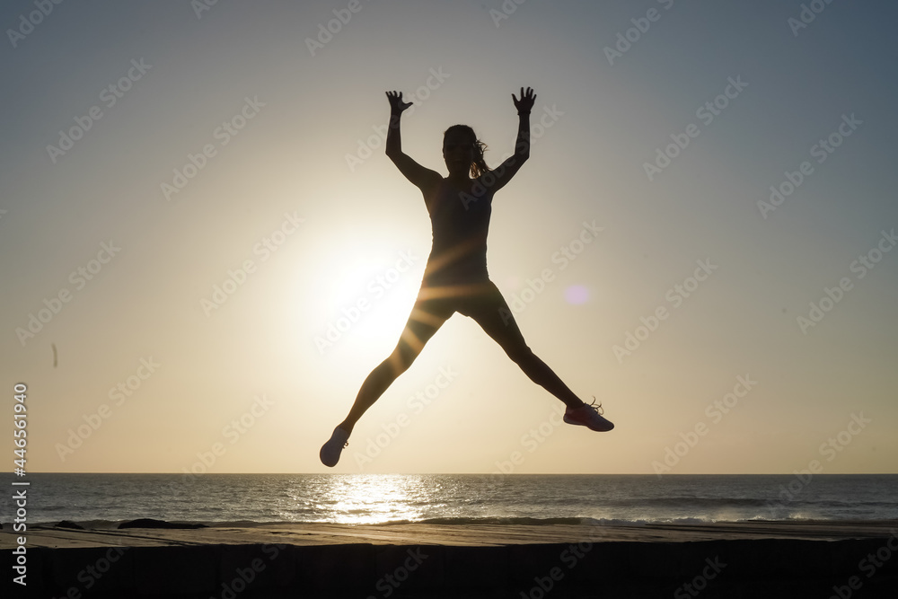 silhouette of a successful  jumping and  joyful woman on beach boardwalk during sunset or sunrise for motivation
