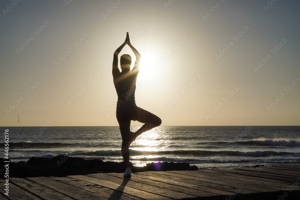 silhouette of a sportive athletic woman doing yoga on beach boardwalk during sunset 
