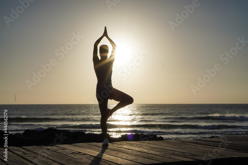 silhouette of a sportive athletic woman doing yoga on beach boardwalk during sunset   © shellygraphy