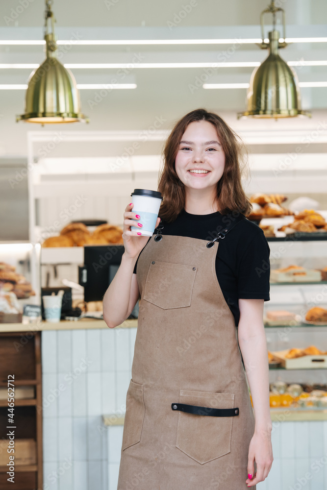 Pretty charming baker girl posing with a plastic coffee cup inside her shop Pretty charming baker girl posing with a plastic coffee cup inside her shop