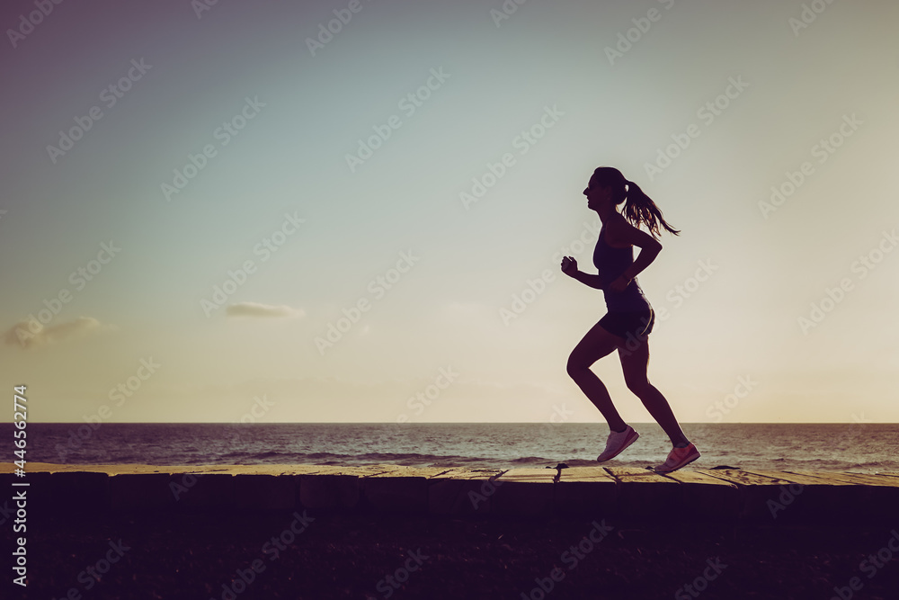 silhouette of a running sportive athletic woman on beach boardwalk during sunset 
