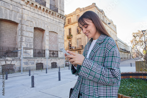 Trendy young woman messaging on smartphone on street photo