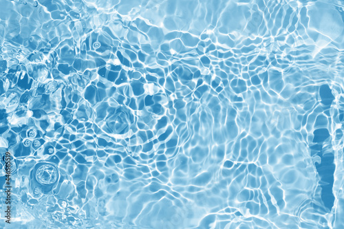 Blurred transparent blue colored clear water surface texture. Water waves in sunlight.