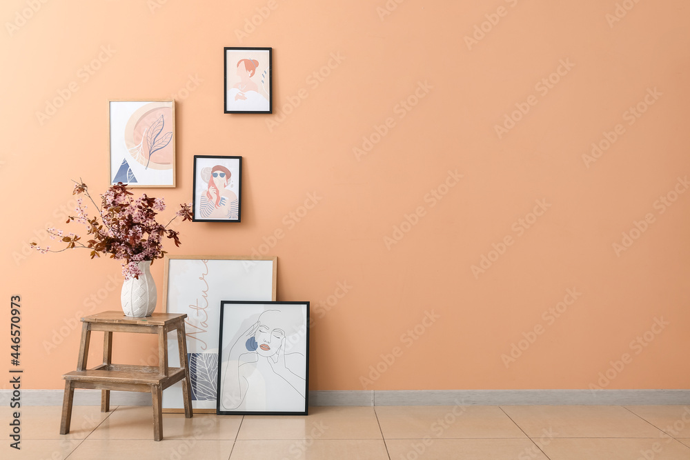 Vase with blossoming branches on table and pictures near color wall