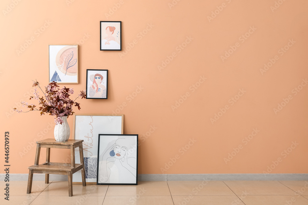 Vase with blossoming branches on table and pictures near color wall Vase with blossoming branches on table and pictures near color wall