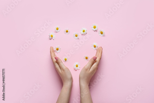 Female hands with heart made of beautiful chamomile flowers on color background