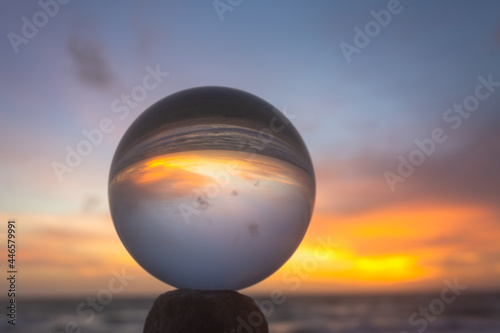 .view on the beach in beautiful sunset inside crystal ball placed on a timber by the sea. .Unconventional and beautiful natural views on the beach and sunset in a magic crystal ball. . © Narong Niemhom