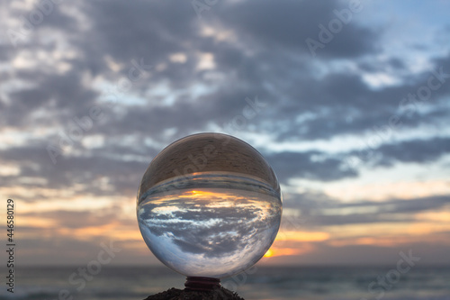 beautiful cloud and golden sunset inside crystal ball placed on a timber beside the beach..beautiful nature in a crystal ball by the sea..Unique and creative travel and nature idea..