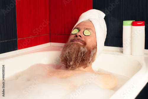 Fotótapéta Cute bearded man taking bath with head wrapped in towel and cucumber slices on his eyes