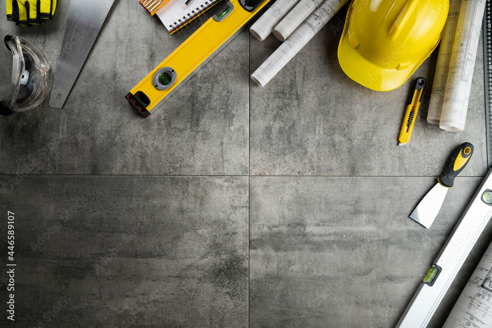 Contractor theme. Plans, tool kit of the contractor, yellow hardhat and libella. Gray tiles background. Contractor theme. Plans, tool kit of the contractor, yellow hardhat and libella. Gray tiles background.