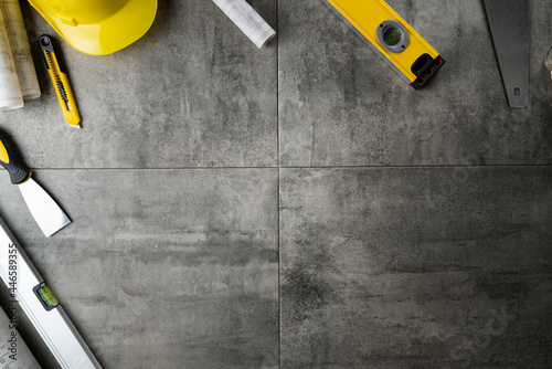 Contractor theme. Plans, tool kit of the contractor, yellow hardhat and libella. Gray tiles background.