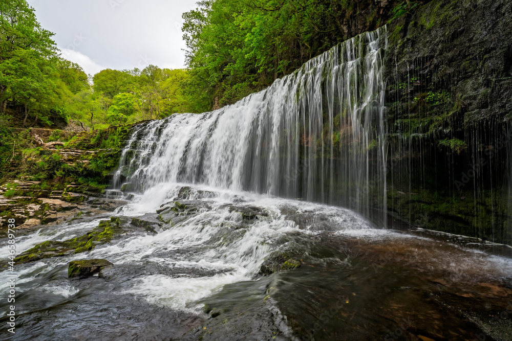 Fototapeta premium Waterfall surrounded by moss, trees, and stones in Ystradfellte Neath UK