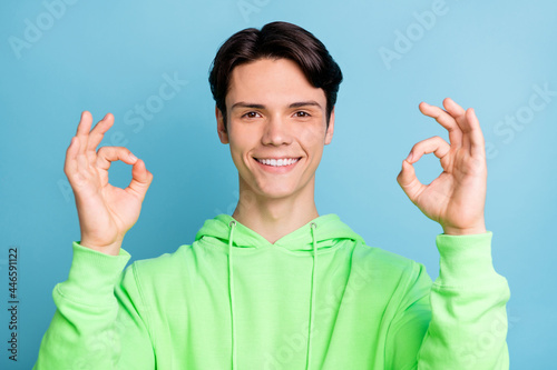 Photo of attractive charming young gentleman wear green sweatshirt smiling showing okey signs isolated blue color background