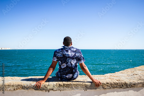 A black man facing the sea along the coast of the city
