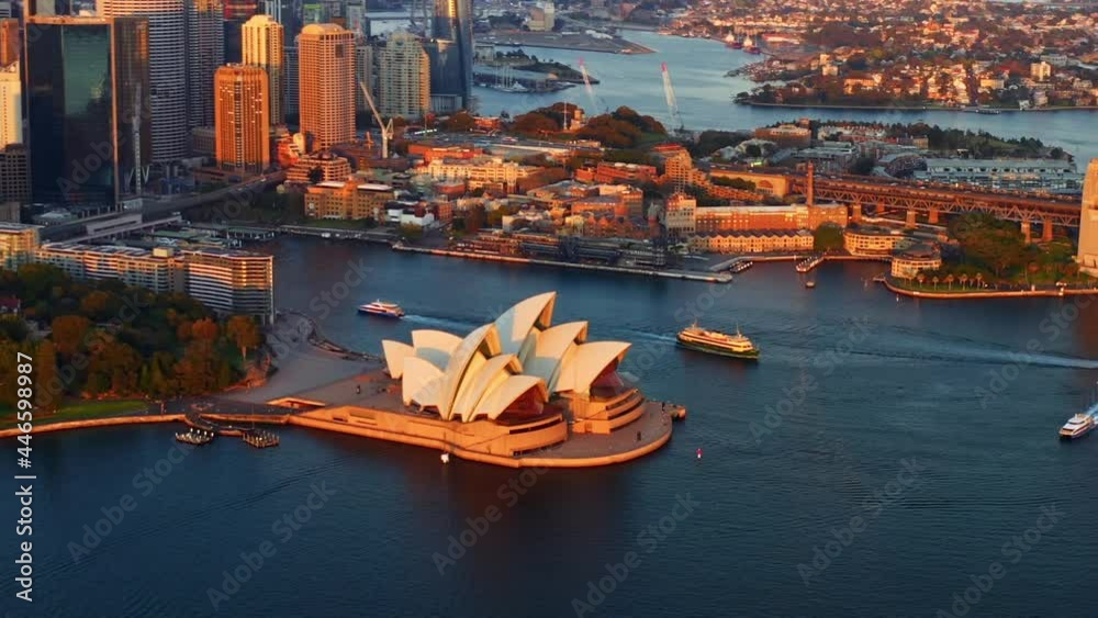 Warm Sunlight Shining On Modern Exterior Of Sydney Opera House With Sydney Skyline In Background. Sydney Harbour In NSW, Australia At Sunrise. aerial pullback