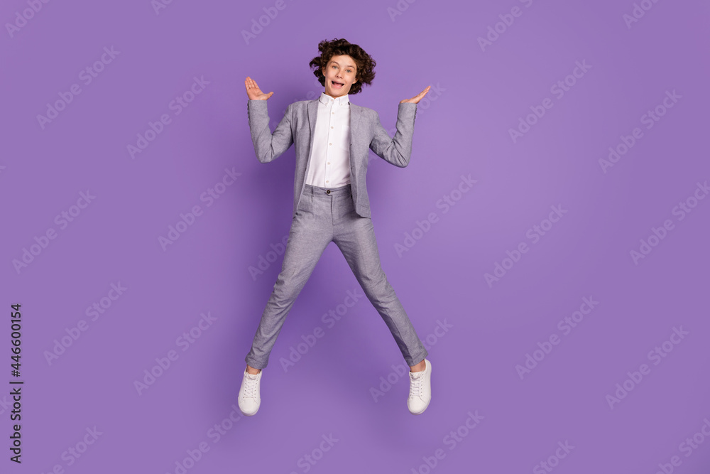 Photo of funny excited crazy kid guy jump raise palms wear grey suit footwear isolated violet color background Photo of funny excited crazy kid guy jump raise palms wear grey suit footwear isolated violet color background