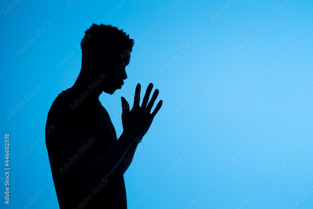 Anonymous black man praying with clasped hands on blue background Anonymous black man praying with clasped hands on blue background