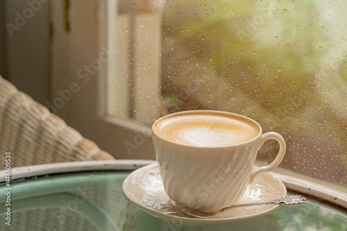 Cup of latte coffee with latte art close to the windows with rain drop