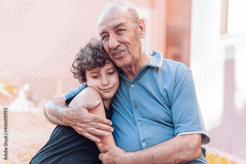 Grandfather hugging his grandson sitting on a bench outdoors. Outside scene.