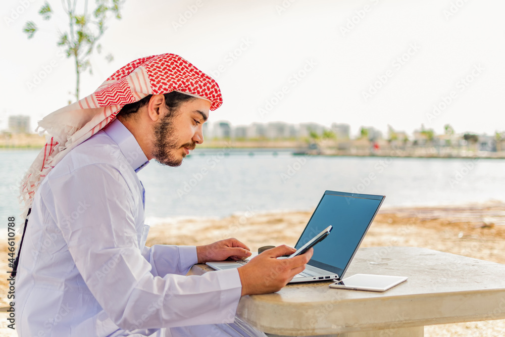 Arab man working on the phone and a laptop at maritime area in Middle East.