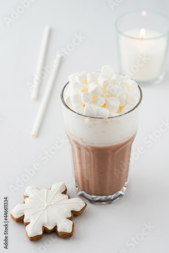 Glass with cocoa, milk froth and marshmallow, snowflake cookies, straws and a burning white candle, a delicious winter drink
