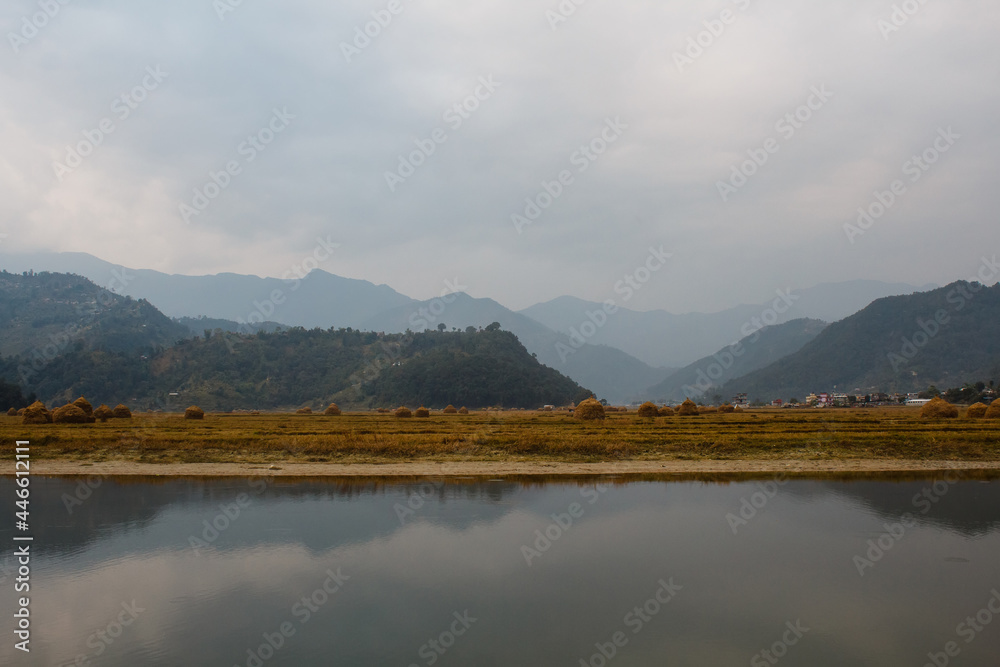 river and fields with harvest in the mountains covered with mist in nepal