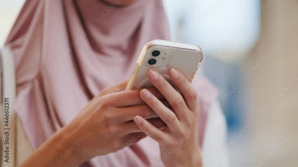 A cropped view of an arabian woman wearing national hijab is using her mobile phone while walking outside on the street