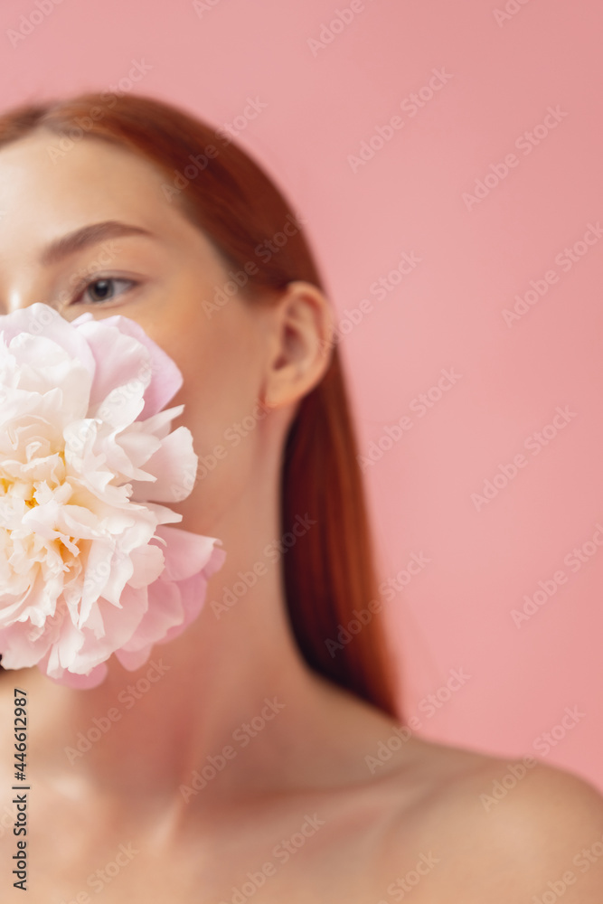 Crop portrait of beautiful redheaded woman with flower isolated over pink studio back ground. Nude color, diet, cosmetics, natural beauty and aesthetic cosmetology concept.