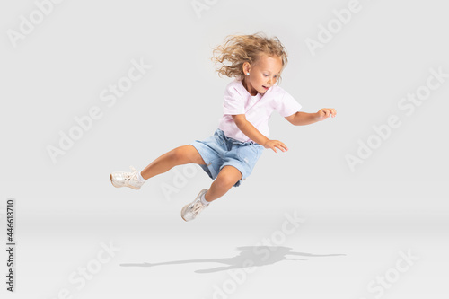 Studio shot of little preschool Caucasian girl in casual clothes falling down isolated over white studio background.