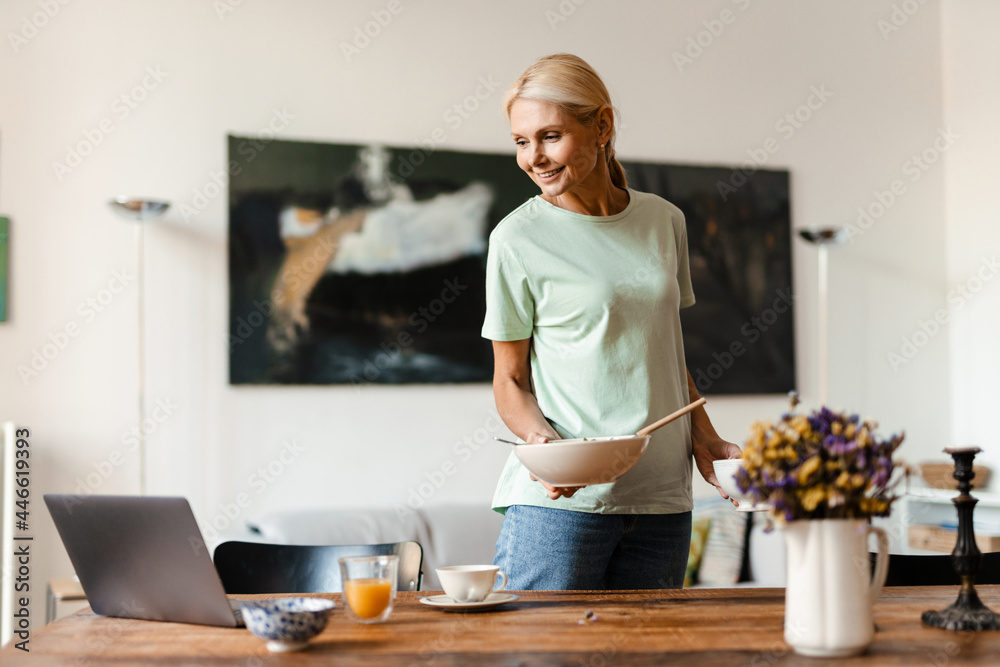 Blonde mature woman using laptop while having lunch at home Blonde mature woman using laptop while having lunch at home