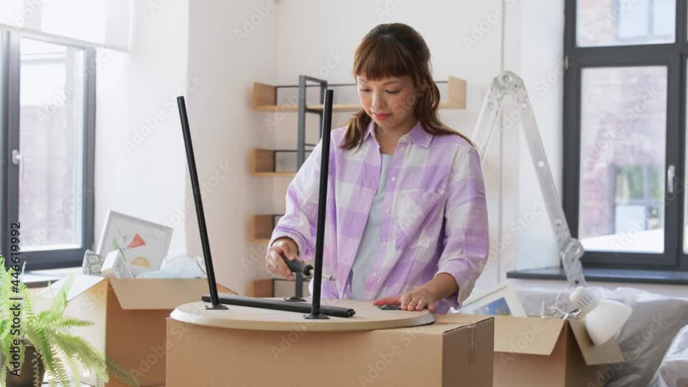 moving, furniture and interior concept - happy smiling asian woman with screwdriver assembling coffee table at new home