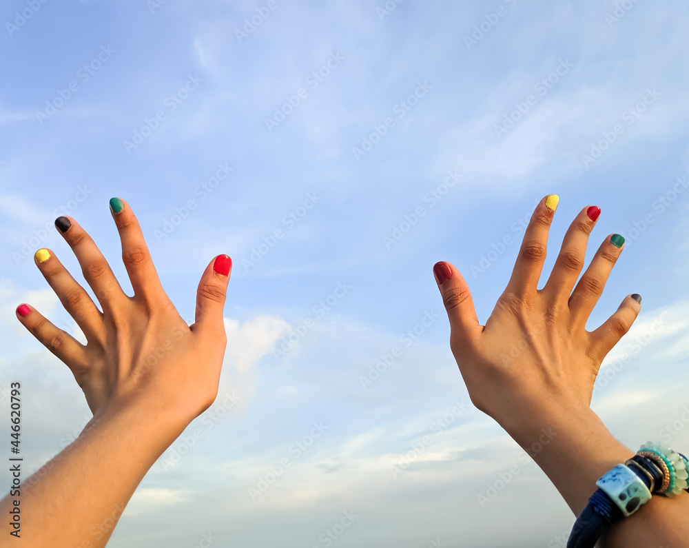Two Brown hands looking like holding something in the blue sky wearing colorful nail polish with space to write your text Two Brown hands looking like holding something in the blue sky wearing colorful nail polish with space to write your text