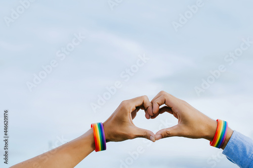 Closeup shot of a gay couple holding hands with a rainbow wristband made hands forming a heart shape in the sky, Concept of LGBT, activism, community, homosexuality, and freedom. photo