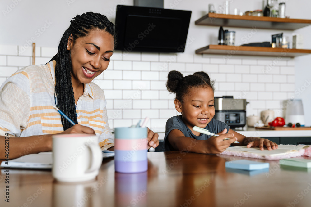 Black woman and her daughter smiling and writing in exercise books