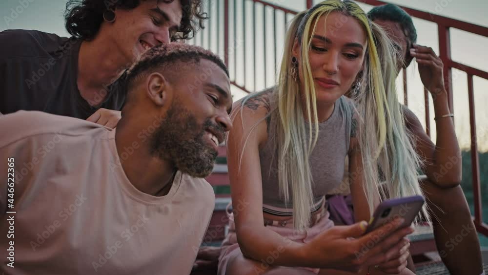 Group of young happy diverse friends spending time together, watching social media on smartphone and laughing, zoom in