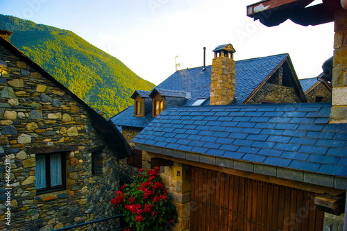 Rural houses with pointed roofs made with stone and wood in a mountainous natural landscape.