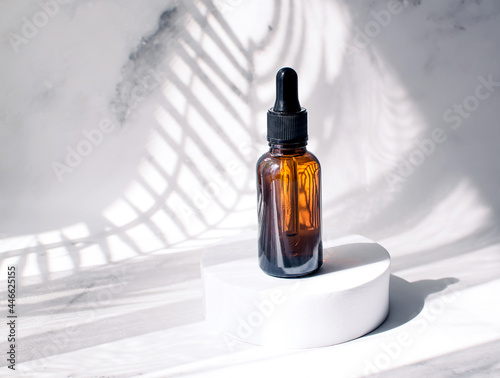 A bottle with cosmetics for the face on the podium, on a white background with shadows from the leaves of a palm tree. Skin care concept. Front view