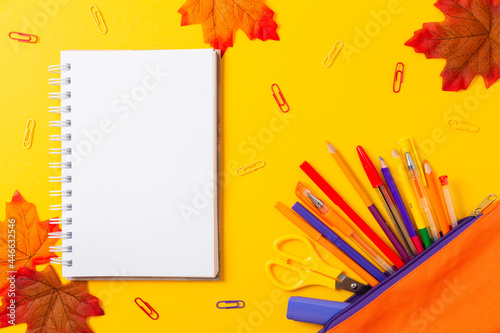 Back to school. Copybook, scissors, clips, pencils and pencil box on yellow background with maple leaves. Flat lay, mock up. Copy space