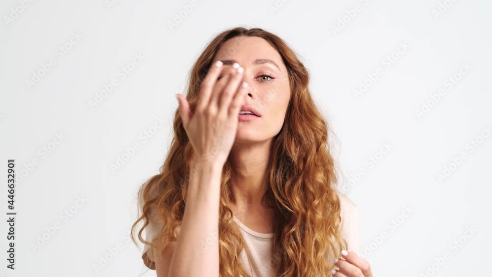 A pleased woman is looking to the mirror while correcting her hairstyle standing isolated over a white wall in the studio A pleased woman is looking to the mirror while correcting her hairstyle standing isolated over a white wall in the studio