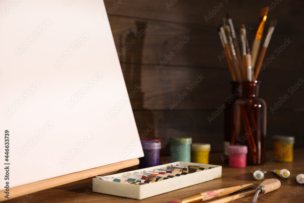 Easel with canvas and art supplies on wooden table Easel with canvas and art supplies on wooden table
