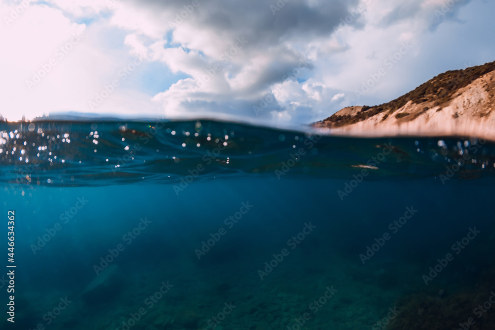 Split shot with coastline and underwater scene with sun rays and transparent sea water.