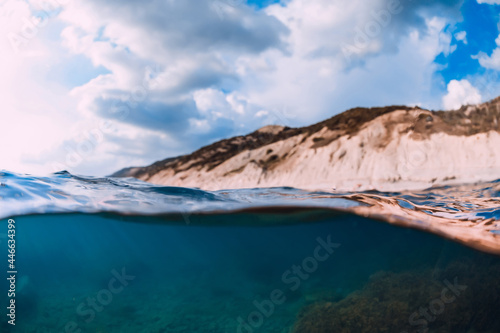 Split shot with coastline and underwater scene with sun rays and transparent sea water.