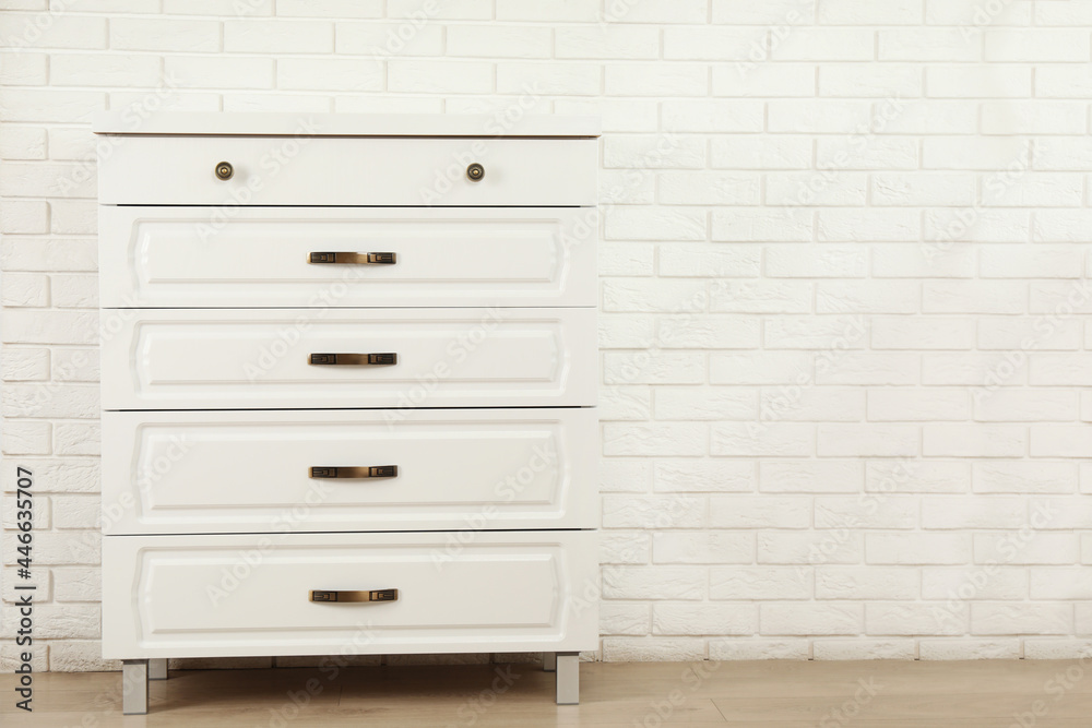 Modern chest of drawers near white brick wall. Space for text