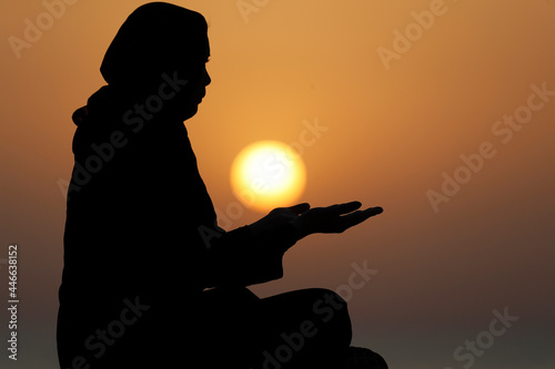 Silhouette of a Muslim woman in abaya praying with her hands at sunset, United Arab Emirates photo