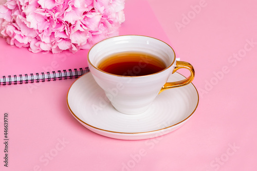 Cup of tea, notebook and hydrangea with copy space on pink background