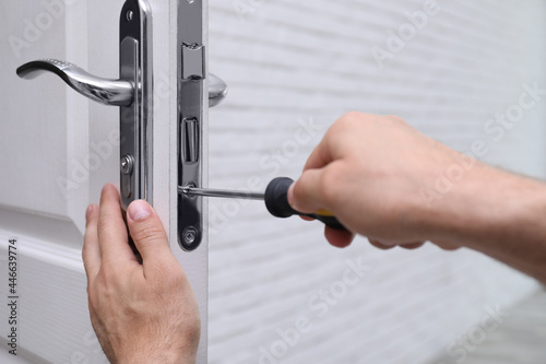 Handyman with screwdriver repairing door lock indoors, closeup