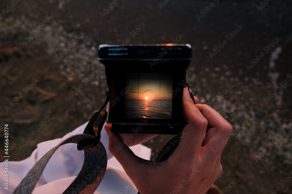 Girl making photo of sunrise over the sea on analog middle format camera.