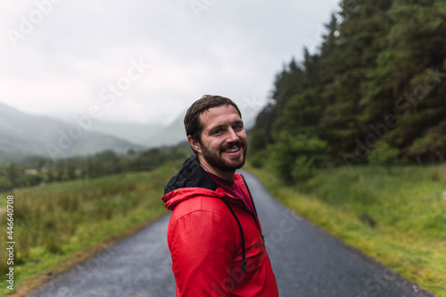 Man in red raincoat walking in an empty road surrounded by a forest during a cloudy day in the Highlands, Scotland
