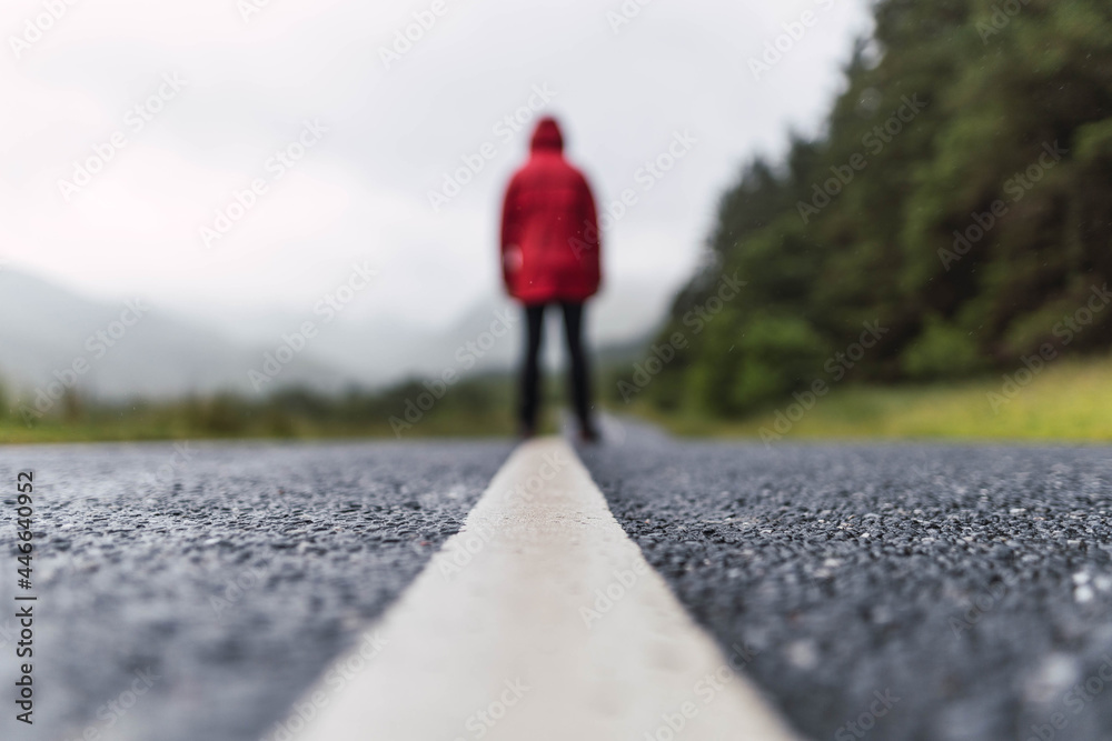 Traveler walking into the horizon on the lonely road in Scotland enjoying the scenery. He is wearing a red raincoat and surrounded by green trees and nature. Enjoying freedom