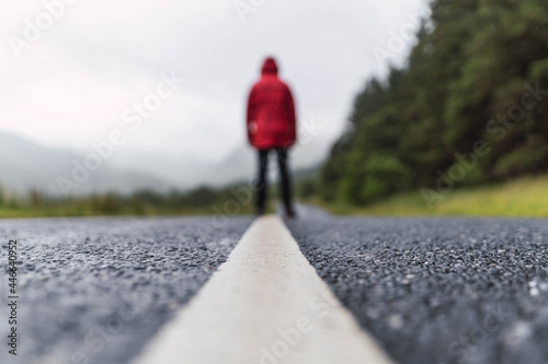 Obraz na płótnie Traveler walking into the horizon on the lonely road in Scotland enjoying the scenery. He is wearing a red raincoat and surrounded by green trees and nature. Enjoying freedom
w salonie